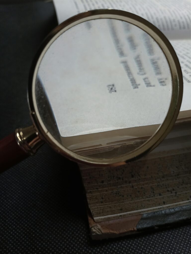 Magnifying glass hovering over an open book, symbolising deep audience research and focused insight into customer understanding.